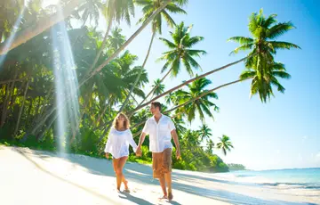 A man and a woman walking on a beach with palm trees